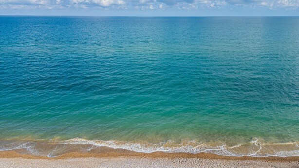 Une plage à l’eau turquoise et limpide, un rivage de galets et un ciel partiellement nuageux.