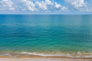 Une plage à l’eau turquoise et limpide, un rivage de galets et un ciel partiellement nuageux.