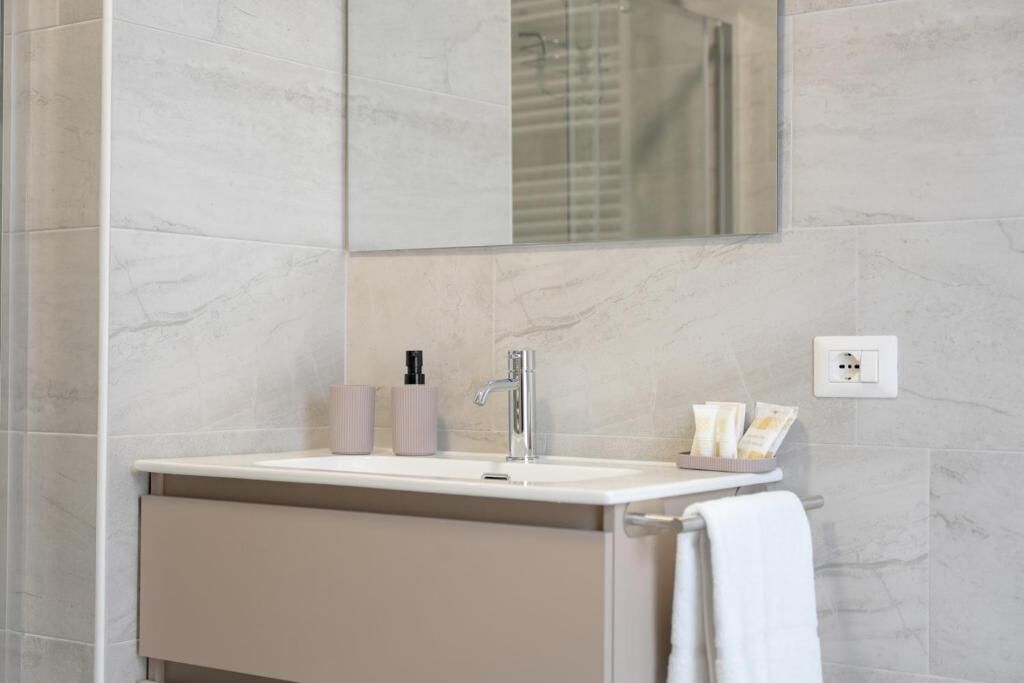Un baño con lavamanos blanco, un espejo, una toalla y artículos de aseo en la encimera.