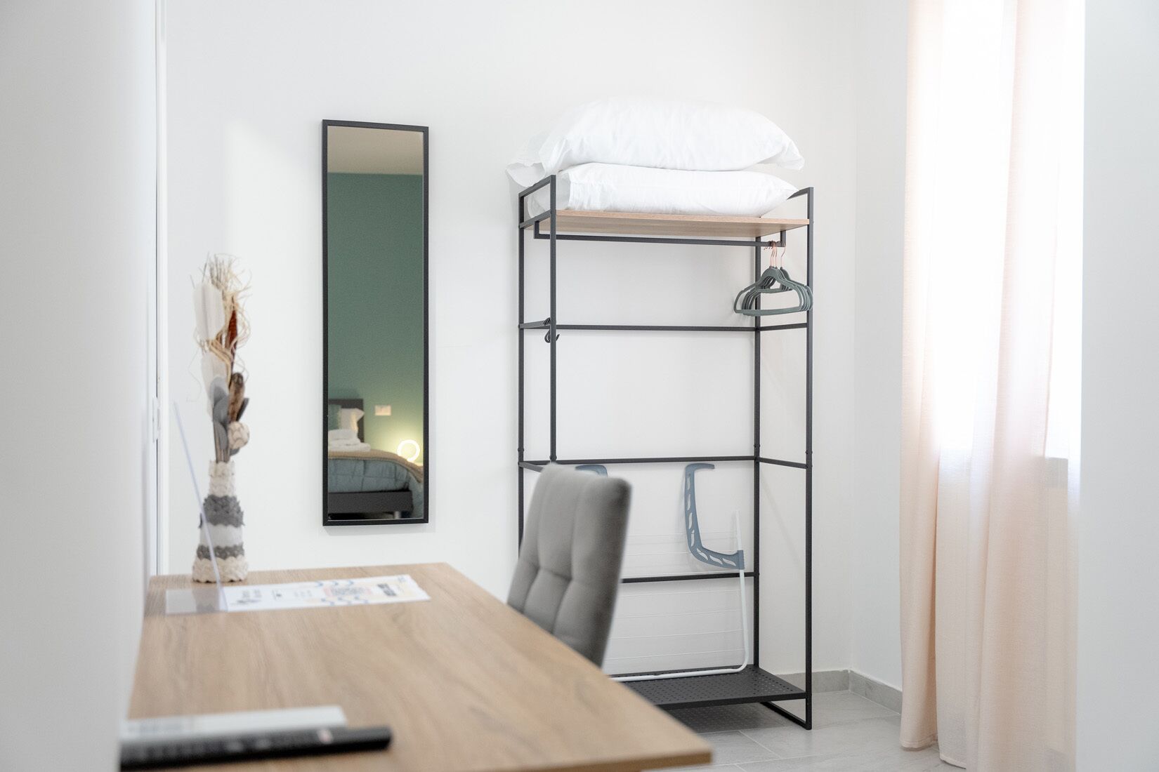 A bunk bed with a mirror, a desk with a chair, and a window with curtains.