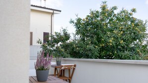 Un balcon avec une table et des chaises en bois, un pot de fleurs et un grand arbuste aux fleurs jaunes.