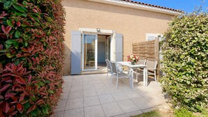Une terrasse avec une table et des chaises, une porte-fenêtre coulissante et une façade de bâtiment de couleur beige.
