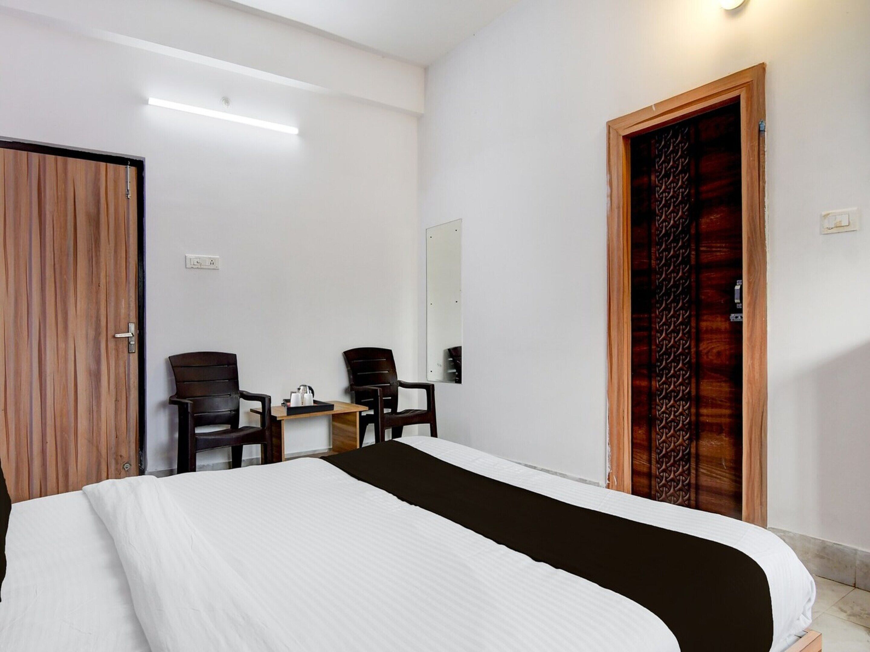 Ein Schlafzimmer mit einem Bett, zwei Stühlen, einem kleinen Tisch, einem Spiegel und einer Holztür.