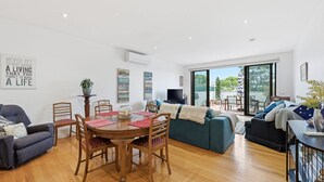 A spacious living area with a dining table, chairs, a sofa, and a balcony with a view. - Tide & Town - Perfectly Located! (Inverloch)