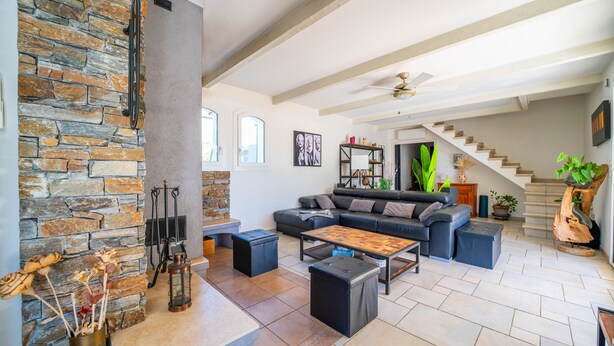 Amplia sala de estar con chimenea de piedra, un conjunto de sofás modernos y una escalera que conduce a un nivel superior.