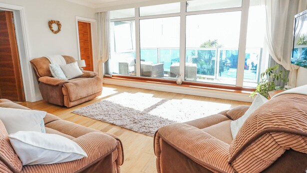 A spacious living room with large windows, a sofa, a chair, and a rug. - Flat 17 Golden Gates (Poole)