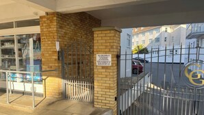 A gated entrance with a sign indicating delivery instructions, a storefront with beach-themed merchandise, and a building with a visible logo. - Flat 17 Golden Gates (Poole)