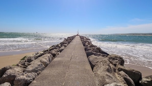 A concrete pier extending into the sea with waves crashing against it, under a clear sky. - Flat 17 Golden Gates (Poole)