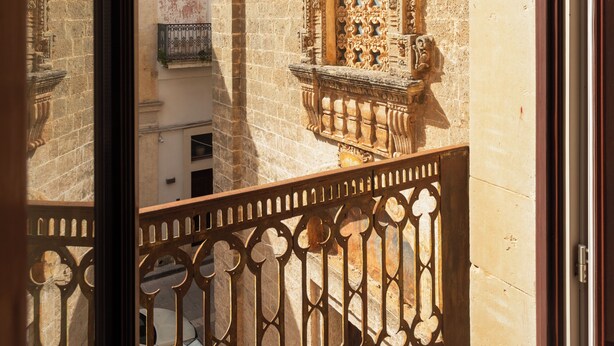 Blick durch einen Balkon mit aufwendiger Steinmetzarbeit und schmiedeeisernem Geländer.