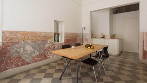 Ein Essbereich mit einem Holztisch, vier Stühlen, einem kleinen Fenster mit Blumen und einer Küche im Hintergrund.