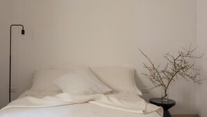 Ein Bett mit weißer Bettwäsche, eine Nachttischlampe und eine Vase mit Zweigen.