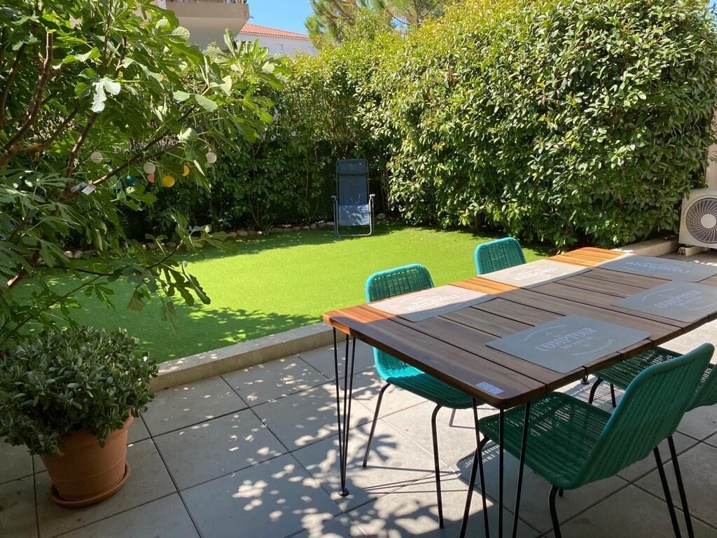 A patio with a wooden table and green chairs, surrounded by lush greenery and a well-maintained lawn.
