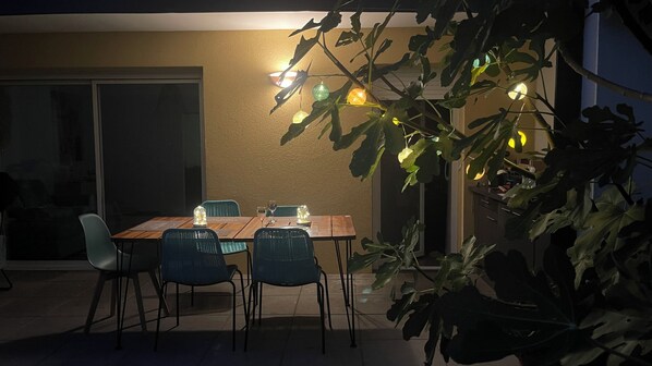 Un espace de restauration en plein air avec une table et des chaises, une plante en pot et un luminaire fixé au mur.