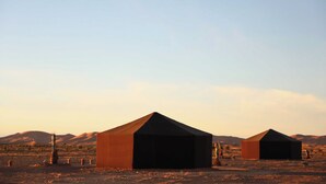 A desert landscape with two large, dark tents. - Hamada Retreat (Tisserdmine)