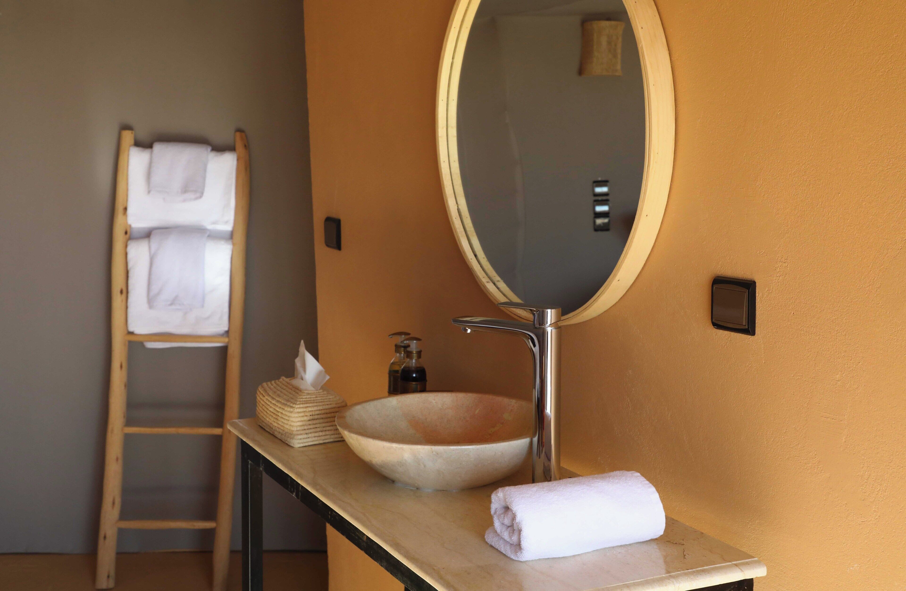 Une salle de bain avec une échelle en bois, un miroir rond, un lavabo beige, une serviette et un distributeur de savon.
