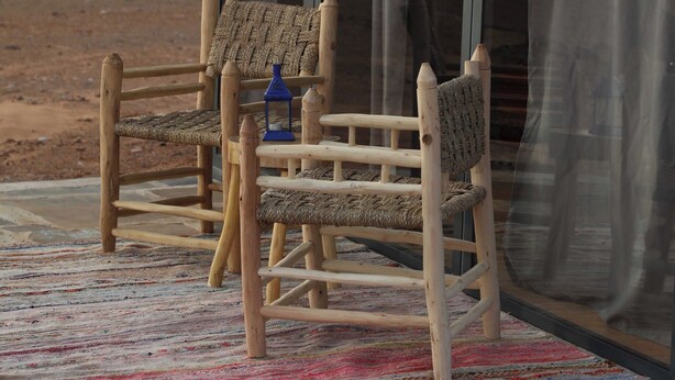 A wooden chair and a small table with a lantern on a colorful rug outside a building with large glass doors. - Hamada Retreat (Tisserdmine)