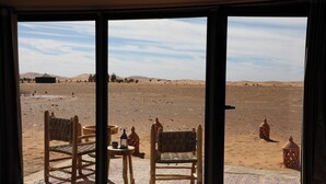 A room with a large window overlooking a desert landscape, featuring two wicker chairs and a small table with a lantern. - Hamada Retreat (Tisserdmine)