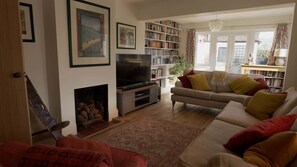 A living room with a sofa, a television, a fireplace, and a bookshelf. - Spacious Home in the Cotswolds, Parking & Garden (Westmancote)