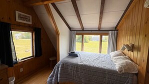 Un dormitorio con cama, paredes de madera, una ventana y techo de vigas de madera.