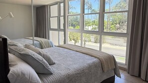 Een slaapkamer met een groot bed, een raam met gordijnen en uitzicht op groen buiten.