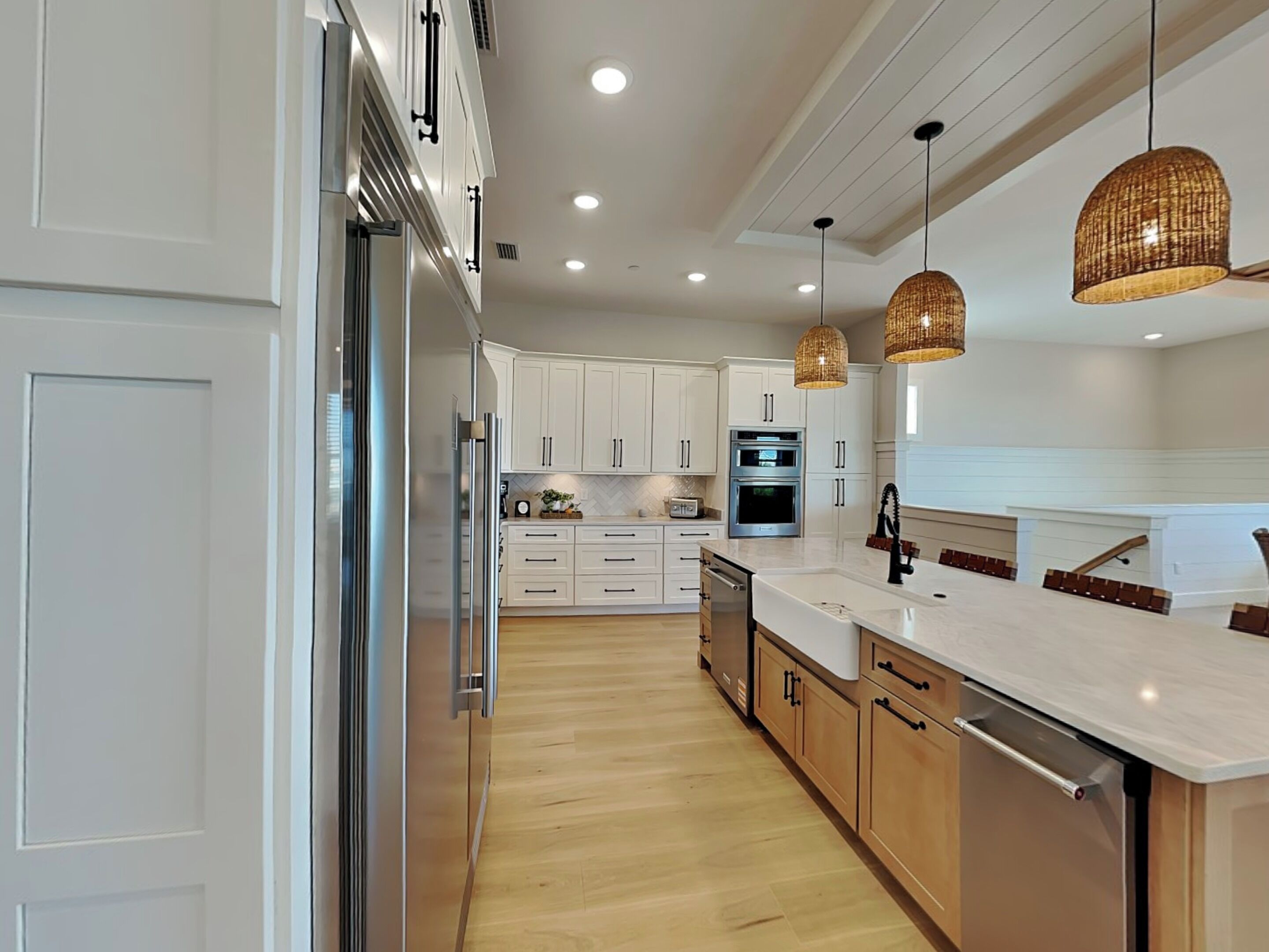 A modern kitchen with white cabinets, stainless steel appliances, and a wooden floor.