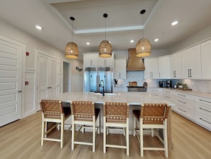 A kitchen with a central island, white cabinetry, and hanging pendant lights. - Salty Seahorse (Panama City Beach)
