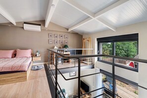 A bedroom with a bed, a desk, a chair, a window, and a balcony with a view of greenery. - Petite house “La Grande Rivière” with pool, Wi-Fi, and air conditioning (Sèvremoine)