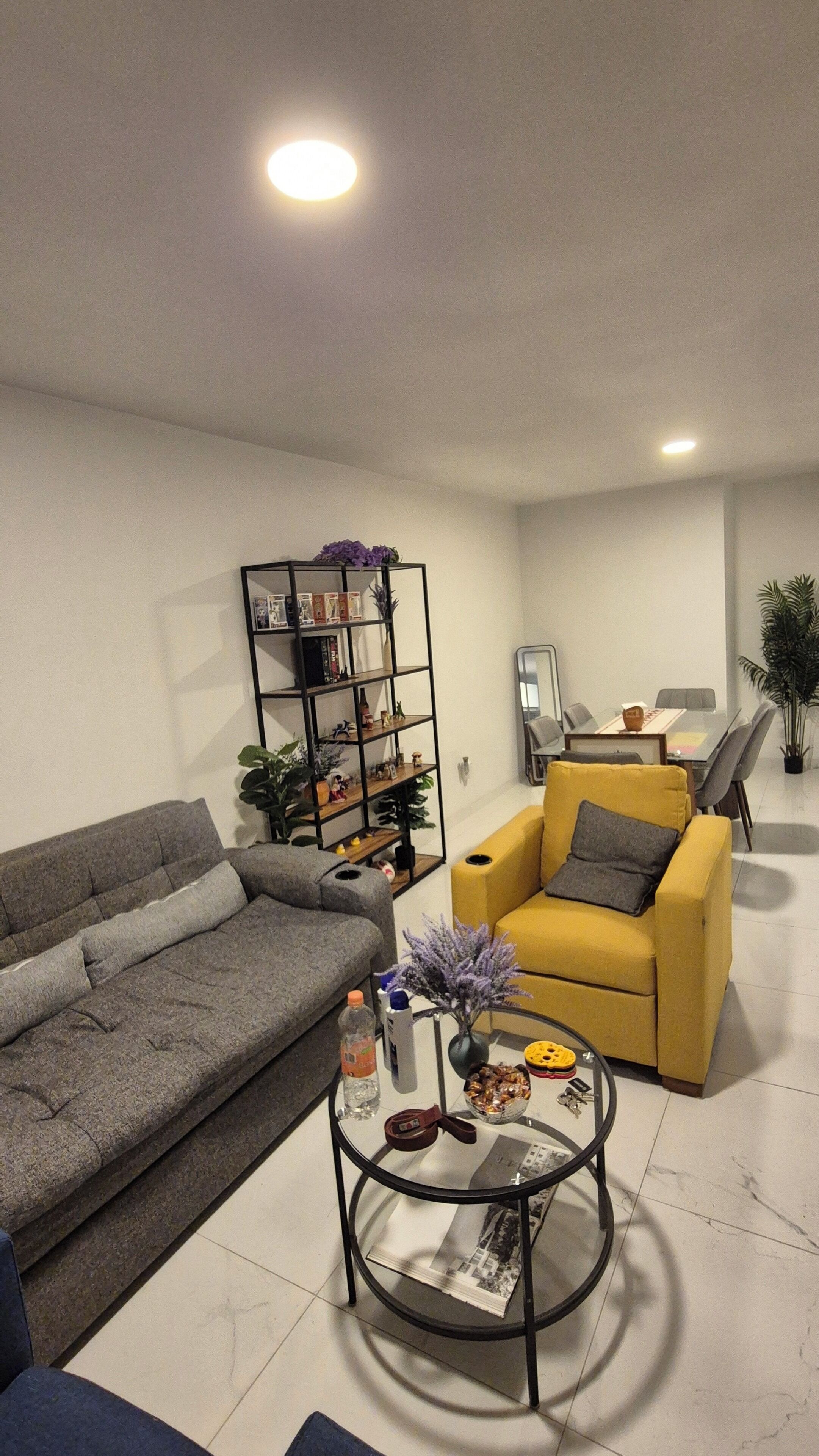 Ein Wohnzimmer mit grauem Sofa, einem gelben Sessel, einem runden Couchtisch und einem Bücherregal.
