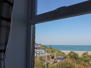 Blick durch ein Fenster auf die Küste mit Strand, Palmen und einem Gebäude mit Außenbereich.