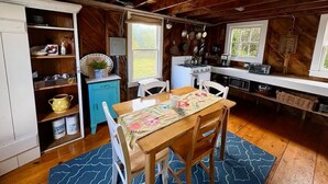 L’intérieur d’un chalet en bois comprend une table à manger, des chaises, un coin cuisine et une fenêtre.