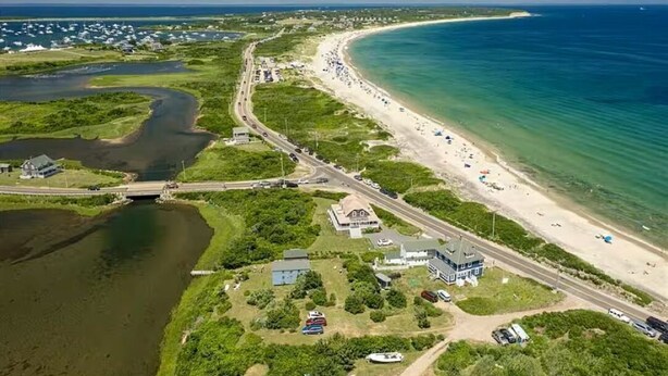 Vue aérienne d’une zone côtière comprenant une plage, une route et une étendue d’eau.