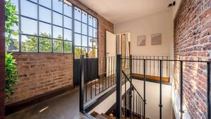 A spacious hallway with exposed brick walls, large windows, and a wooden staircase with black railings. - MOT Rentals + Dorrego House - Pool in Palermo Hollywood (Buenos Aires)
