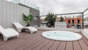 Una terrazza sul tetto con vasca idromassaggio, poltrone relax e una pianta in vaso.