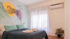 Een slaapkamer met een bed, kussens, een deken en een muurschildering.