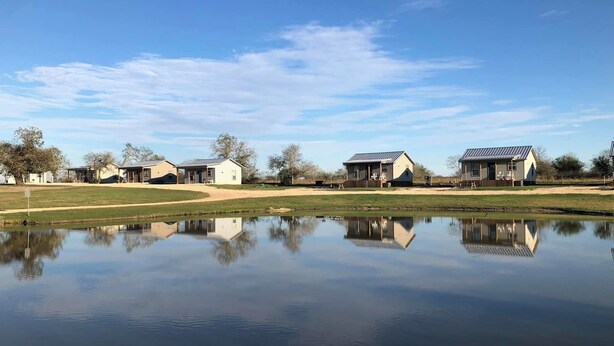 Um cenário tranquilo à beira de um lago, com várias casas, céu claro e superfície da água calma refletindo os edifícios.