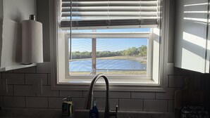 Uma cozinha com janela, pia e uma garrafa de detergente.
