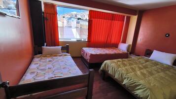 A room with two beds, a window with red curtains, and a view of buildings outside.