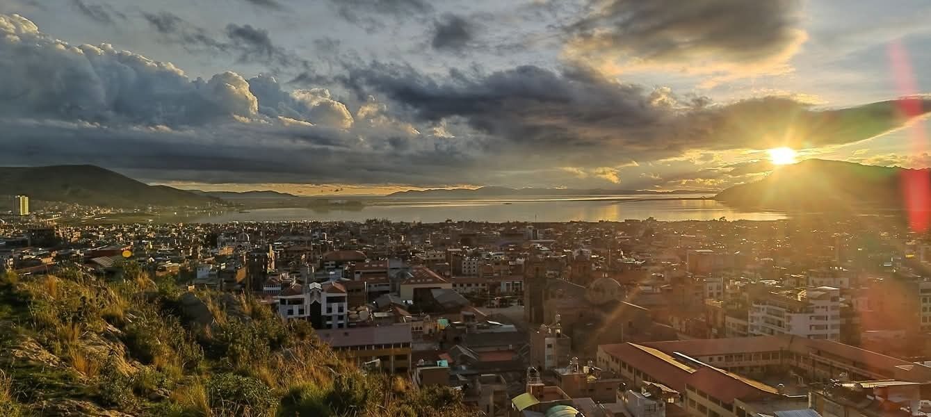 Paisatge urbà amb edificis, una massa d'aigua i muntanyes al fons.