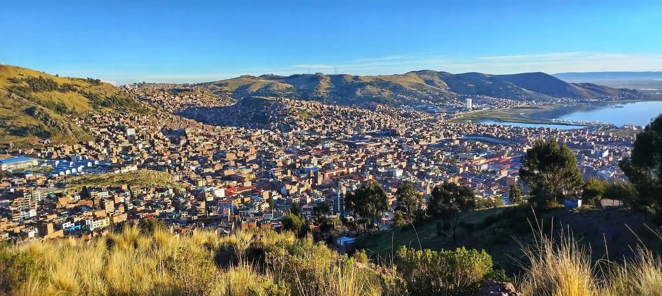 Vista panorámica de una ciudad con un trazado urbano denso, una extensa masa de agua y colinas circundantes.