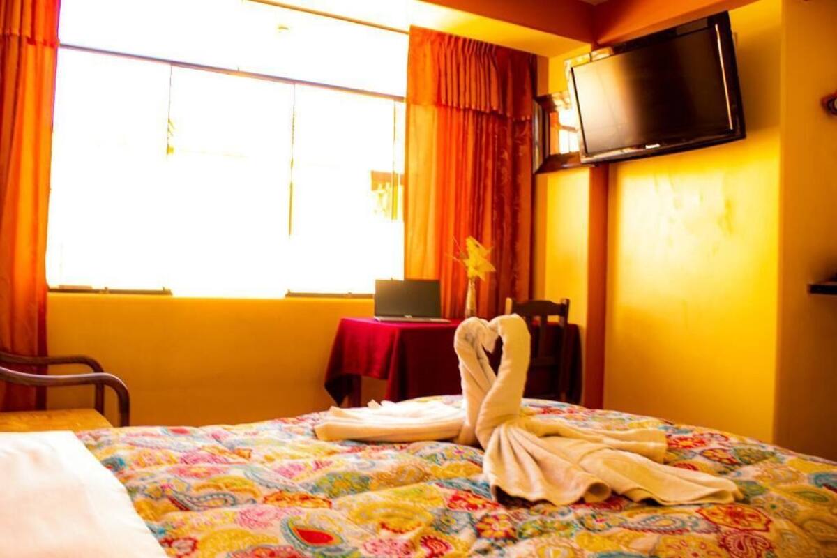 Una camera d'albergo con un letto, una scrivania con un portatile, una televisione a muro e una finestra con tende.