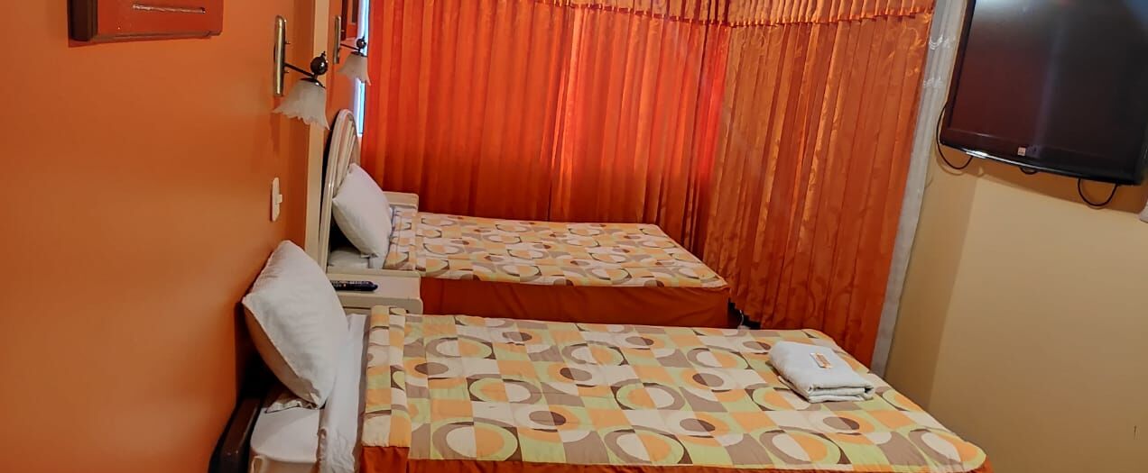 Een kamer met twee bedden, een televisie en een raam met gordijnen.