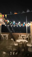 Un patio al aire libre con mesas y sillas, luces colgantes y vistas de la ciudad por la noche.