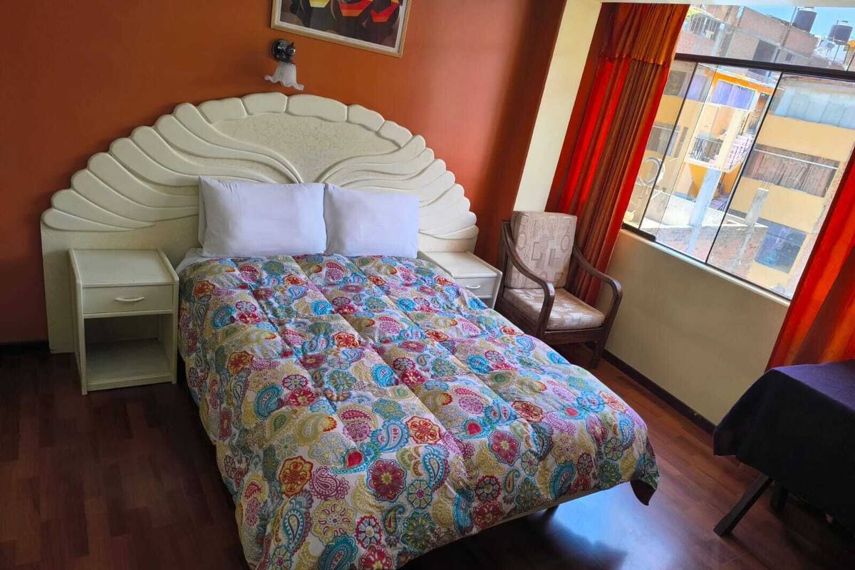 Una camera da letto con un letto, una sedia, un comodino e una finestra con tende.