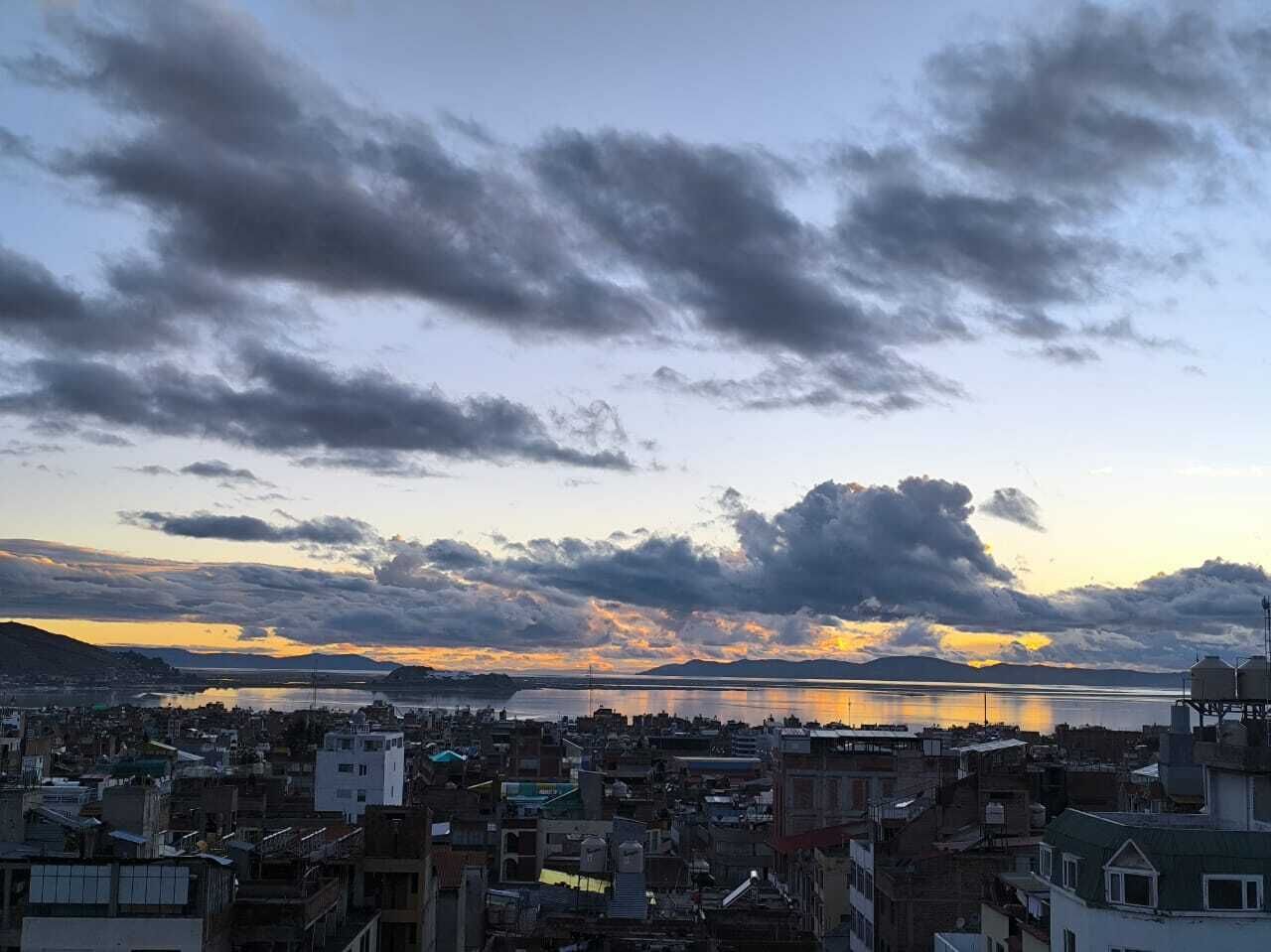 A cityscape with buildings, a body of water, and a sunset sky.