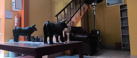 Une pièce avec un escalier, une table ornée de figurines d’animaux, un extincteur et une étagère avec des verres.