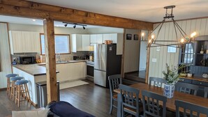 A modern kitchen with white cabinets, a central island with stools, a dining area with a wooden table and chairs, and a cozy seating area with a sofa. - Lovely 4-bedroom cabin in the heart of Sylvan Lake - 4 min walk to the beach (Sylvan Lake)