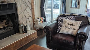 A cozy living room with a fireplace, leather sofa, and a coffee table with remote controls. - Lovely 4-bedroom cabin in the heart of Sylvan Lake - 4 min walk to the beach (Sylvan Lake)