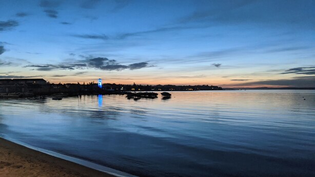 A calm waterfront with a distant illuminated tower, a sandy beach, and a calm sea. - Lovely 4-bedroom cabin in the heart of Sylvan Lake - 4 min walk to the beach (Sylvan Lake)
