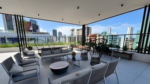 A rooftop terrace with modern seating, a round table, and a view of the city skyline. - Move Oásis Tambaú (Joao Pessoa)