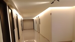 A long, narrow hallway with doors on one side and a wall with a light fixture on the other. - Move Oásis Tambaú (Joao Pessoa)